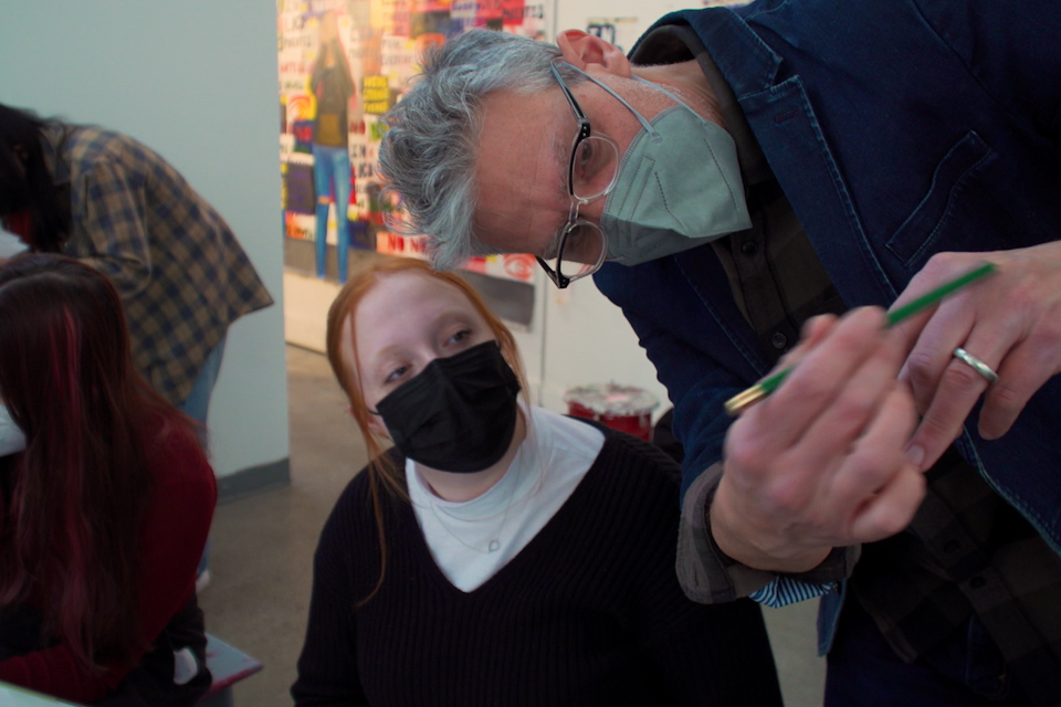 Joe Wardwell wearing a mask, leaning over to show a masked student something in class.