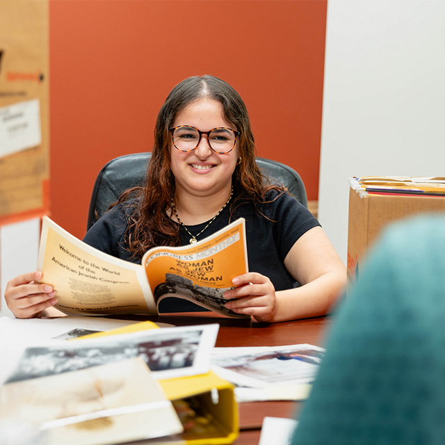Gabriella sits at a table holding a magazine