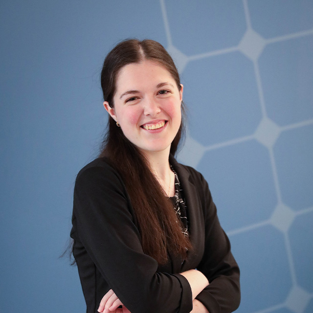 Lauren stands in front of a blue background smiling at the camera