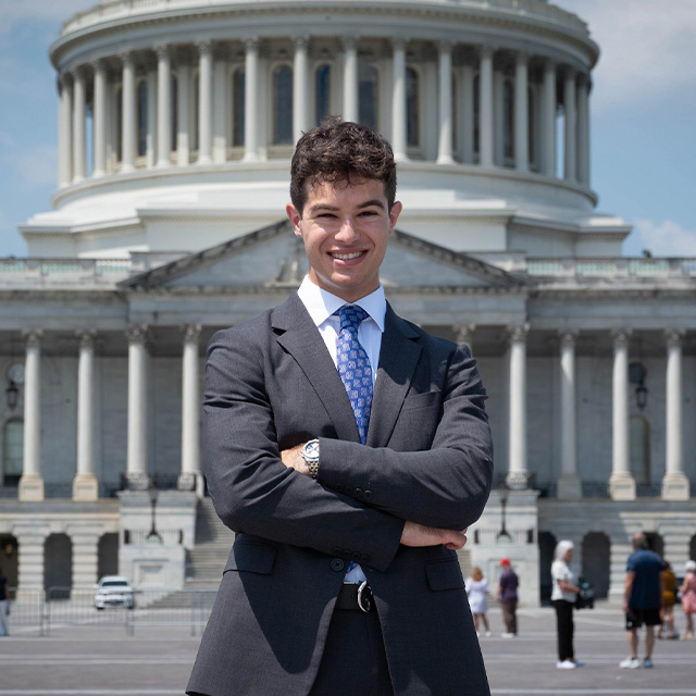 Noah standing with his arms crossed in front of the U.S. Capitol building