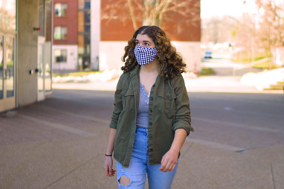 Lydia walks through campus wearing a mask
