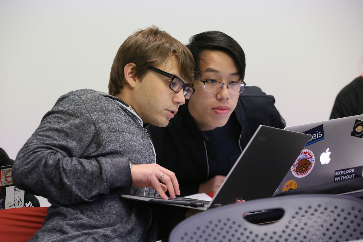 Two students work together on their laptops during class
