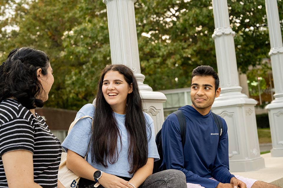 Three students sitting at the base of the Light of Reason outdoor art installation