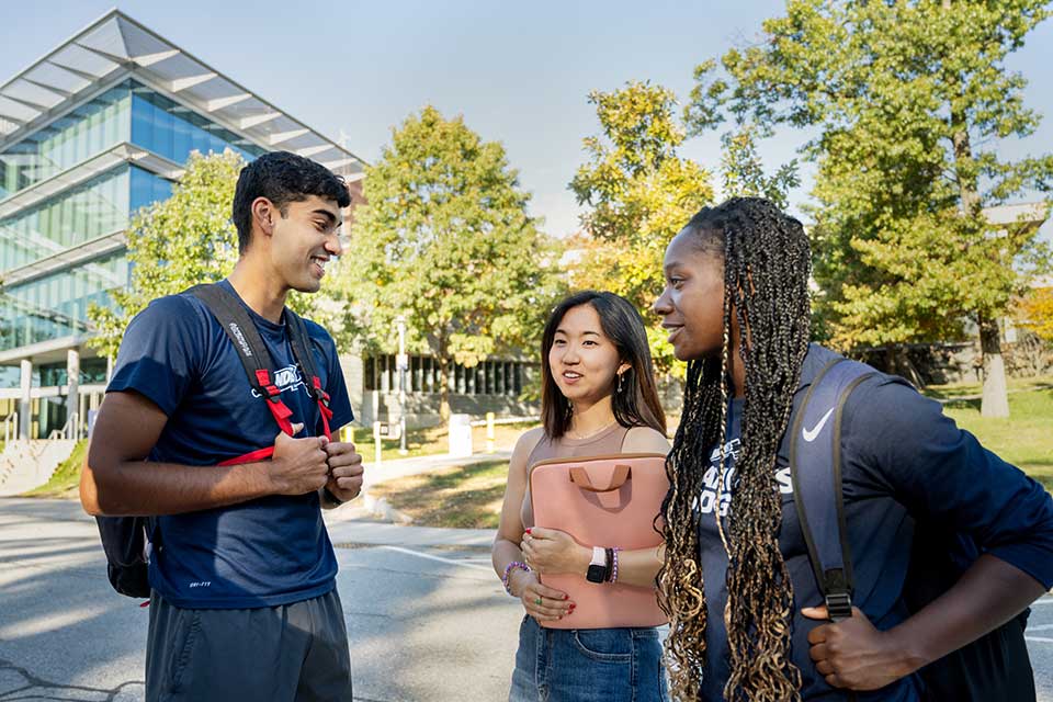 Three students talking outside with the Mandel Center for Humanities in the background