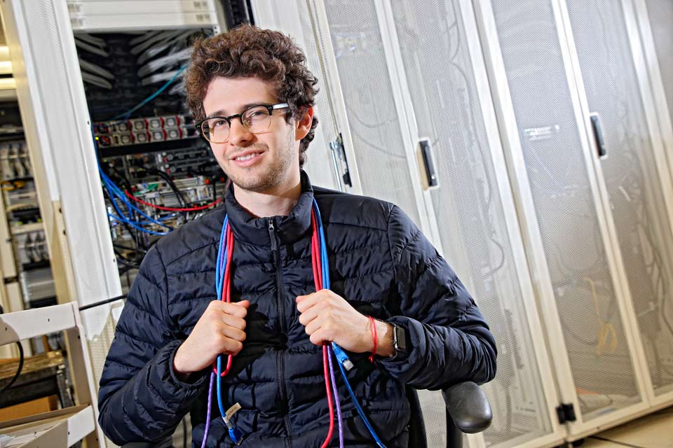 Facundo smiling at the camera, holding computer cords around his neck