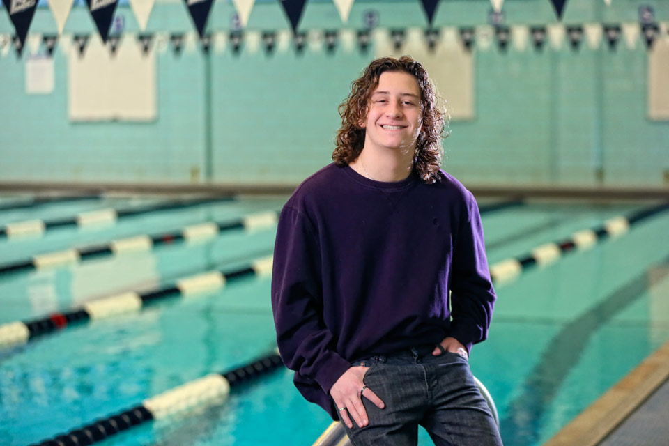Fischer smiling at the camera while sitting on the ladder railing on the side of the indoor pool