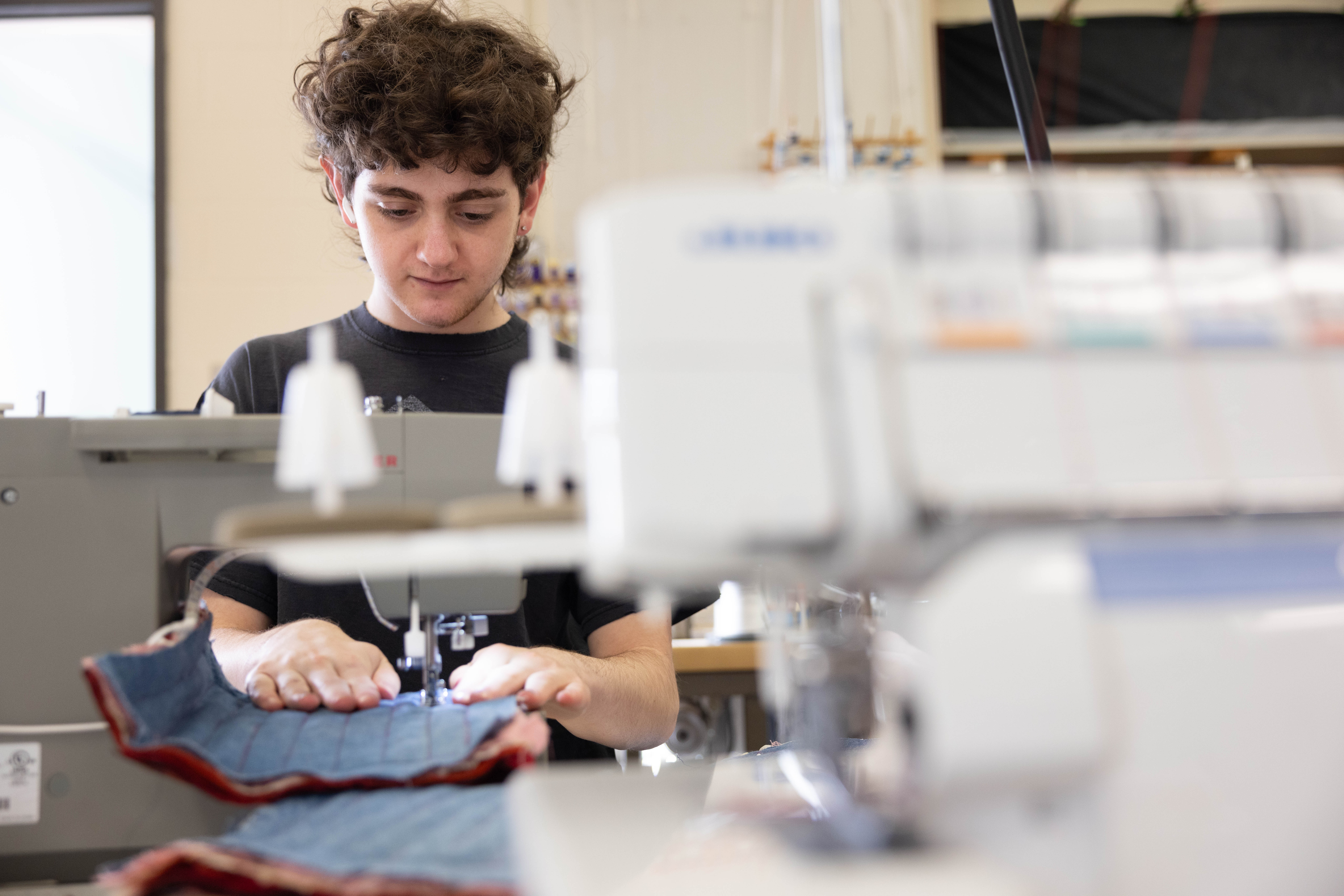 Sam ’27 sews some recycled denim as part of the Indigo Road project, an art installation that tells the story about how the iconic American garments blue jeans were historically made.