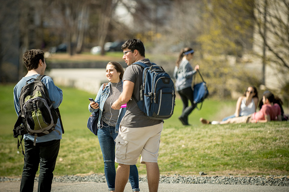 Small groups of students socializing outdoors, some with backpacks, others wearing sunglasses