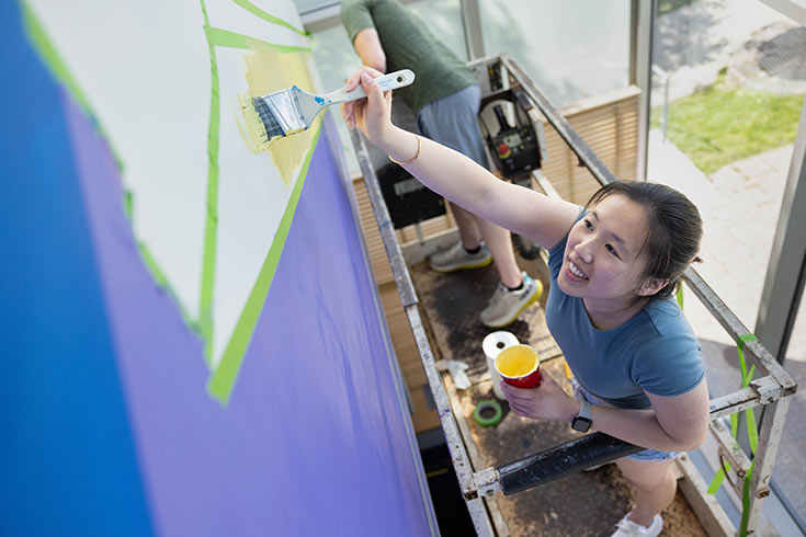 A student using yellow paint to create a mural