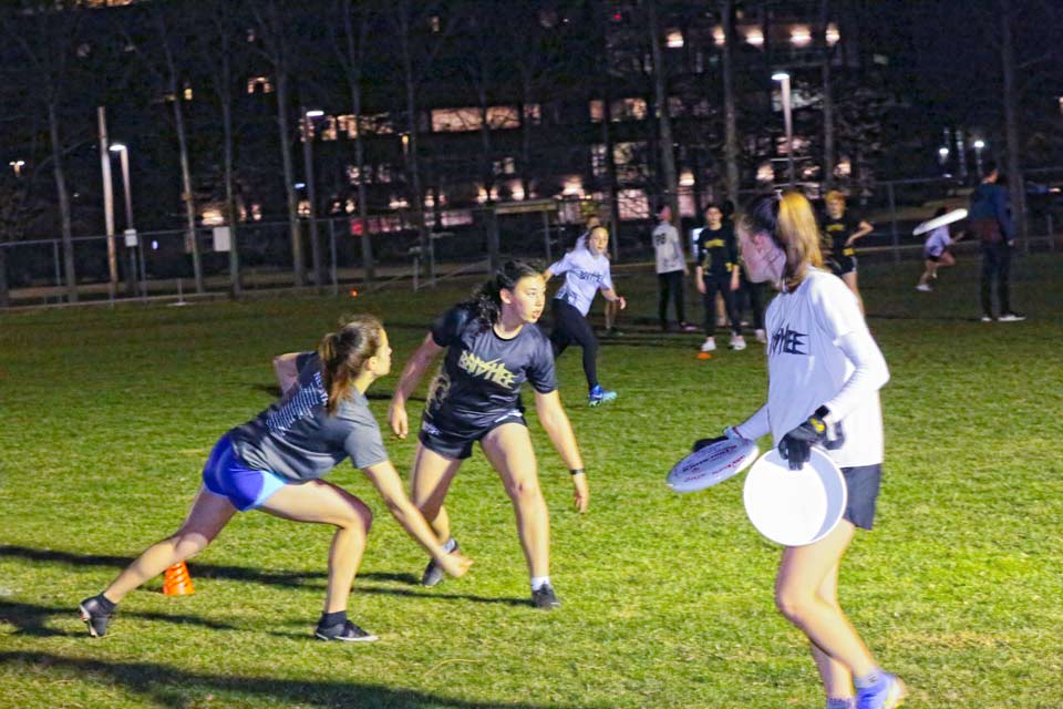 Banshee players on a lit field at night. One player is holding two frisbees.