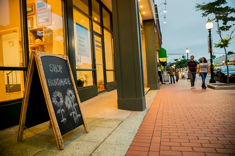 Moody Street in Waltham at dusk; hand chalked sign reads "Shop Handmade" above flowers.