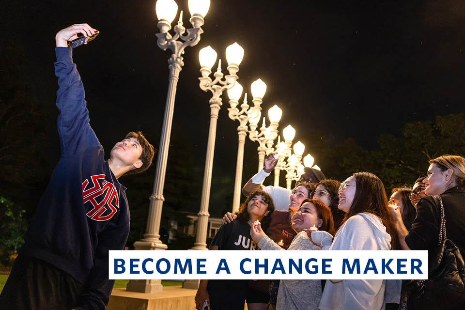 A group of students take a selfie under a row of street lights. Overlay text reads "Become a Change Maker."