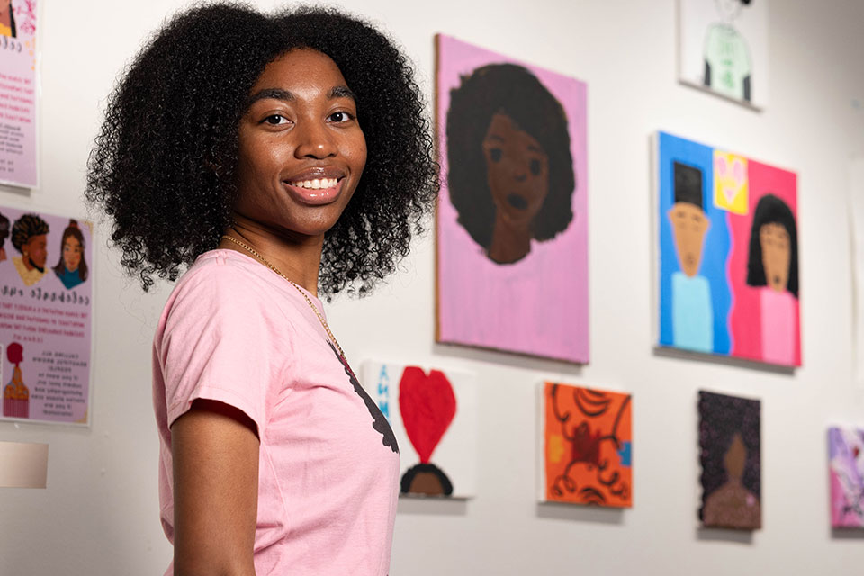 Jolecia smiles in front of a wall of paintings