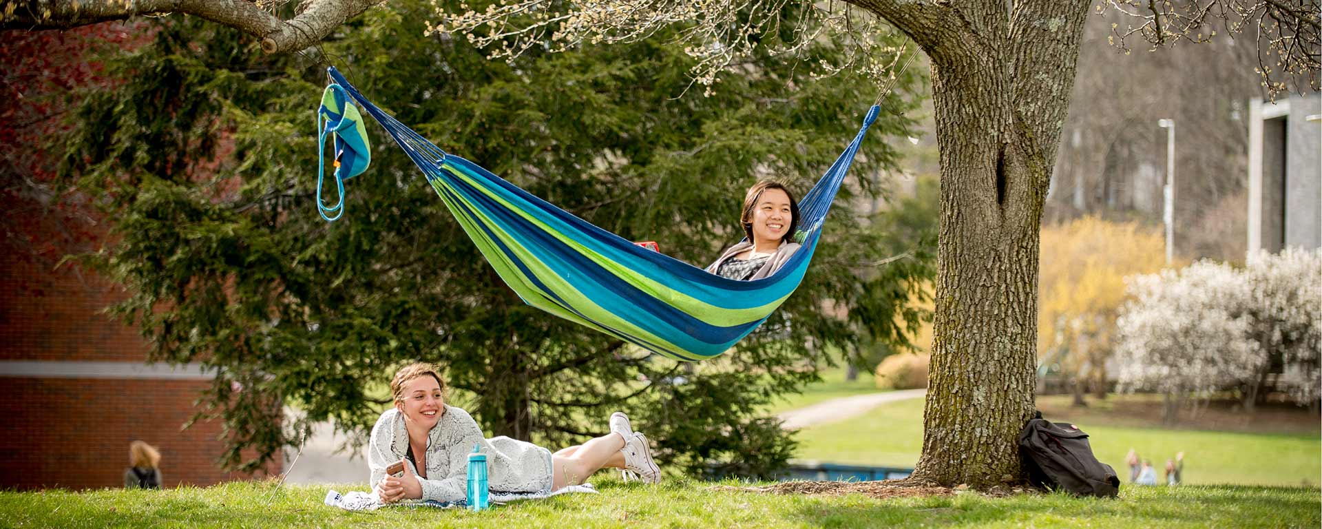 Two people smiling, one in a hammock, one laying in the grass
