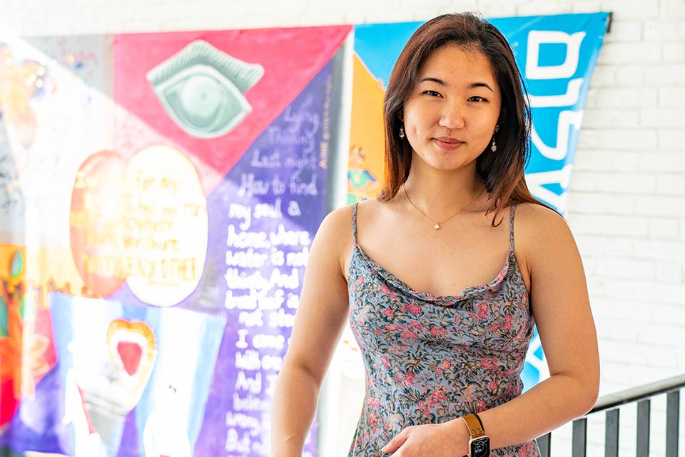 Hannah smiling at the camera, standing in front of a colorful banner