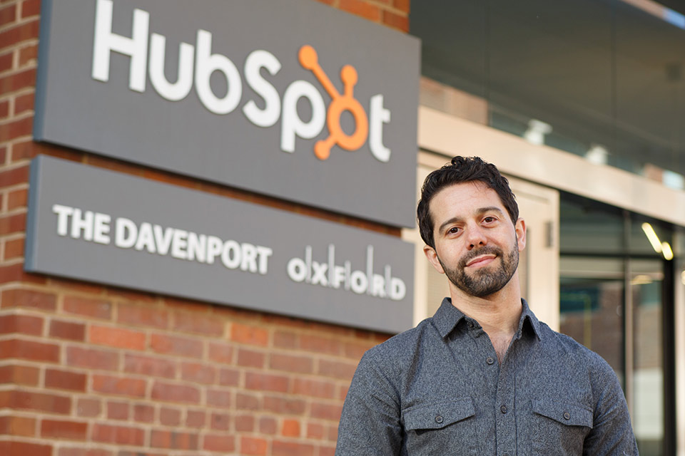 Sam standing outside an office building with the Hubspot logo on the side of the building