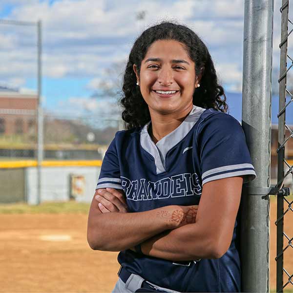 A Brandeis athlete smiles while leaning against a fence