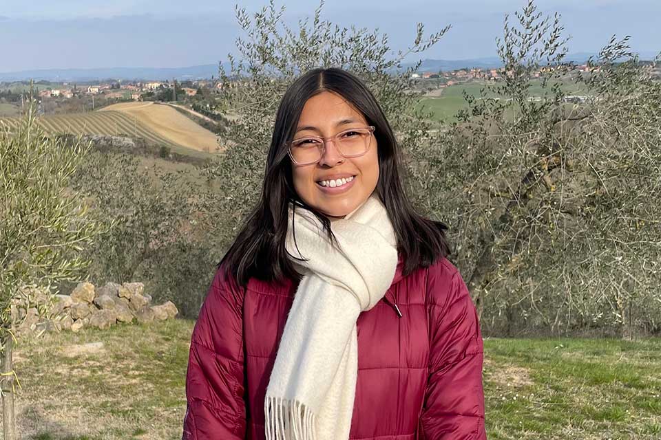 Alex smiling at the camera with rolling hills in the background. She is wearing a coat and winter scarf