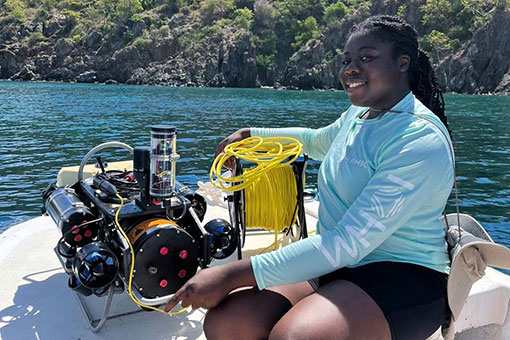 Ianna smiles on a boat next to a robot that she used to visually assess corals and gauge their health.