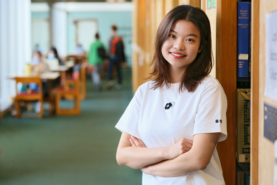 Tianyi in standing in the library, smiling with arms folded