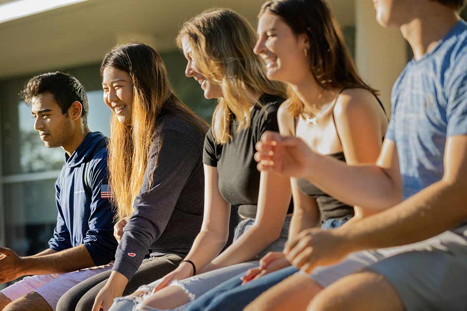 Students smiling, sitting together on a wall on campus