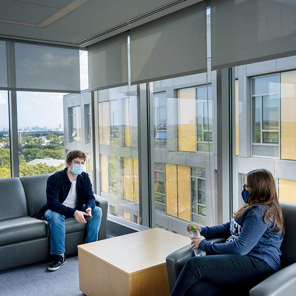 Two students in masks sit and talk in a lounge in Skyline Residence Hall