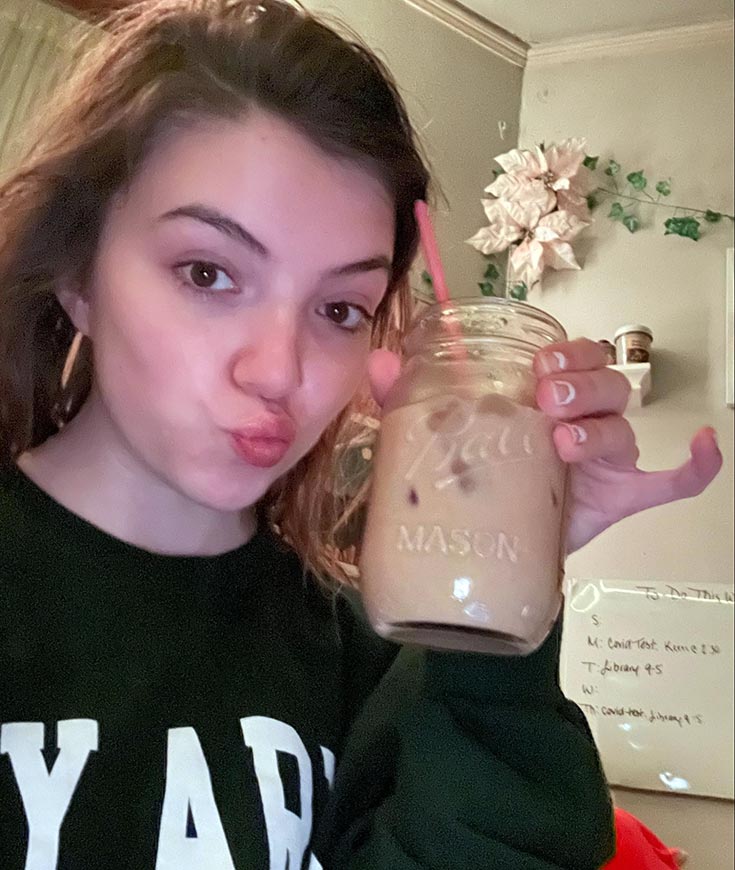 Madison with puckered lips, and holding a mason jar of iced coffee with a straw.