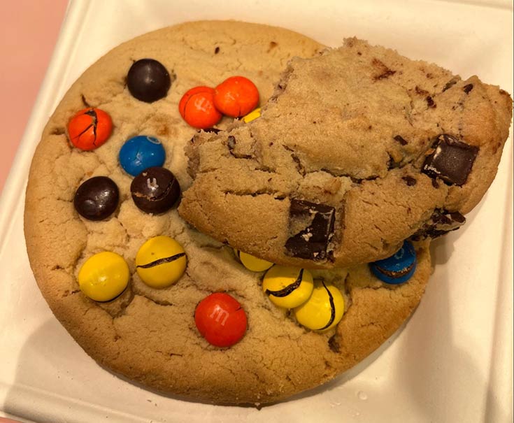 A partially eaten chocolate chunk cookies rests on top of an M&M cookie.