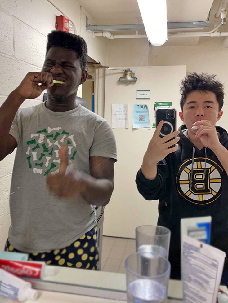Marcus and his roommate brushing their teeth, looking in the bathroom mirror