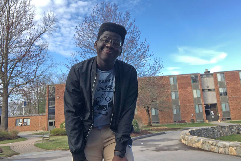 Marcus smiling at the camera while standing outside with a residence hall in the background