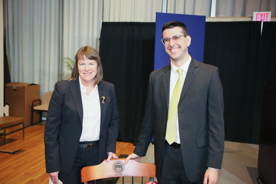Provost Lisa Lynch and Alexander Kaye pose behind a chair with the Brandeis seal.