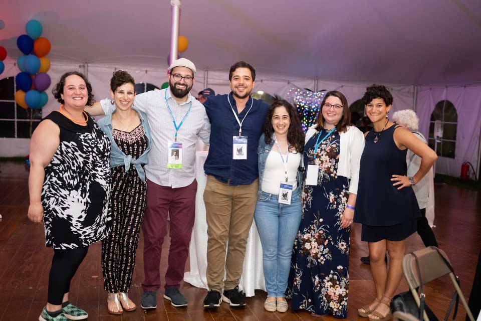 A group of young alumni with arms around each, posing inside a tent.