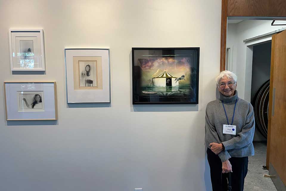 Female artist posing next to works in alumni art gallery