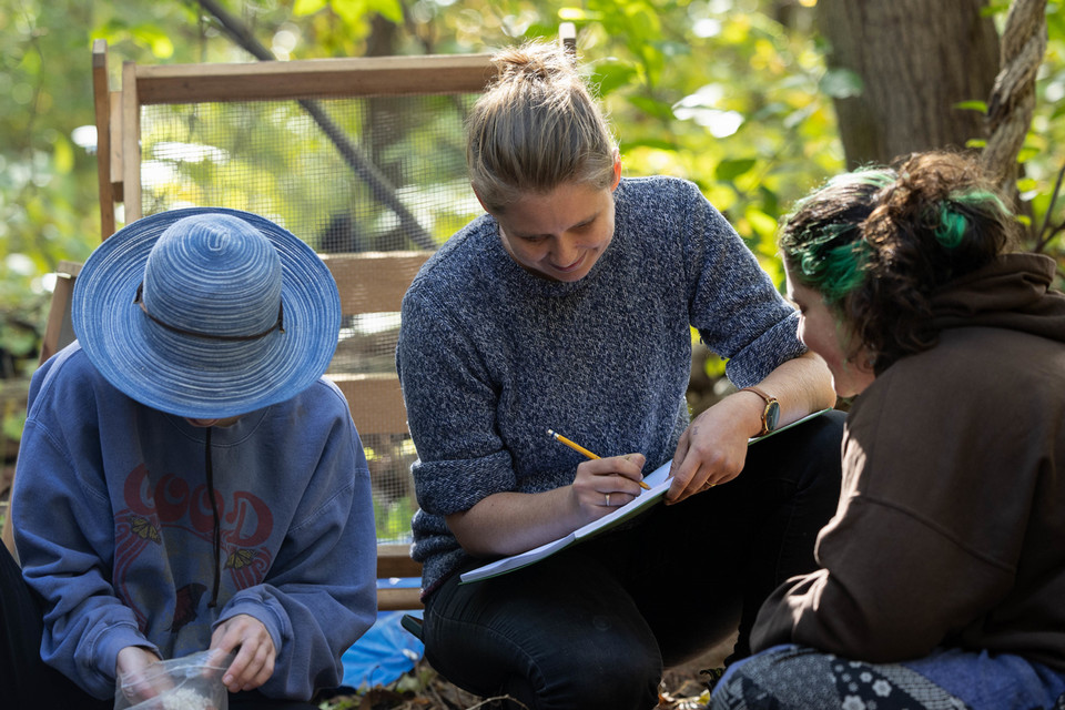 professor writing in notebook outside with students working beside her