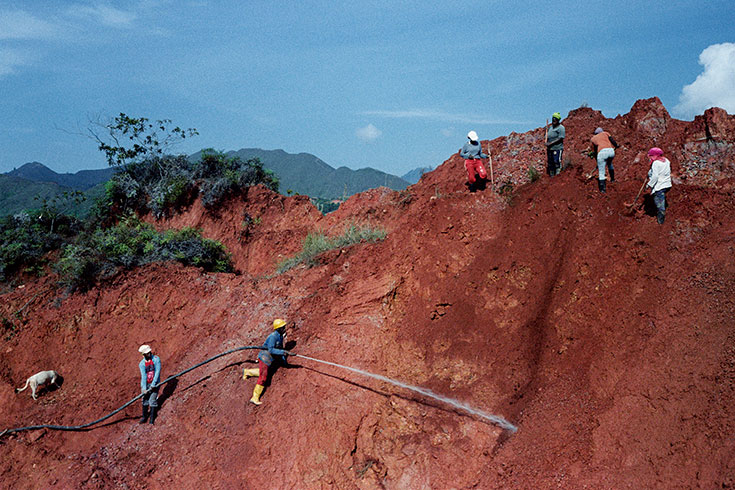 Workers dig and spray water on a very large hill.