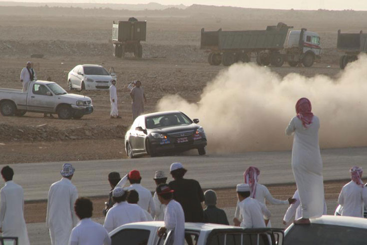 A car kicks up dust while group of people look on in Saudi Arabia
