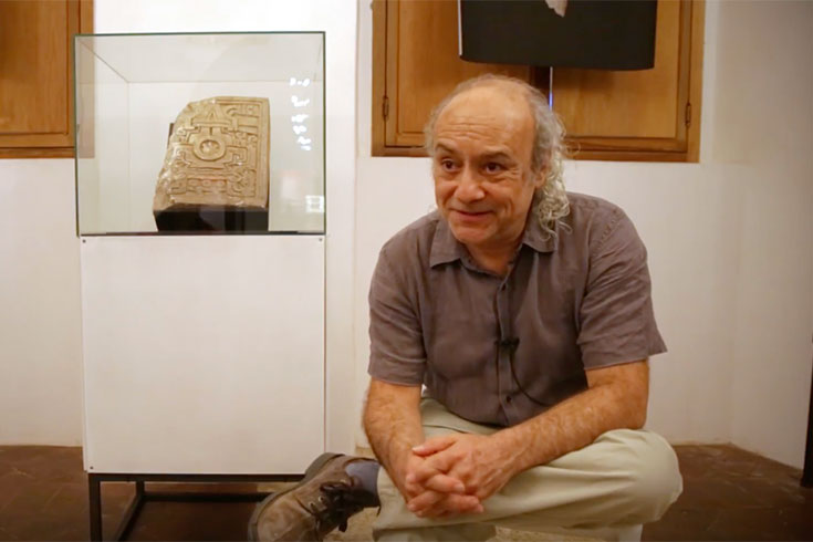 Javier Urcid sits during an interview, in front of some artifacts