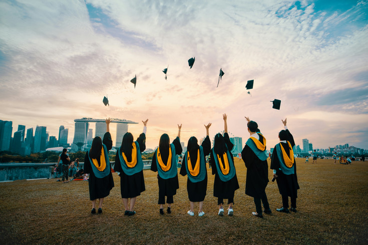 students in graduation gowns throwing caps in the air