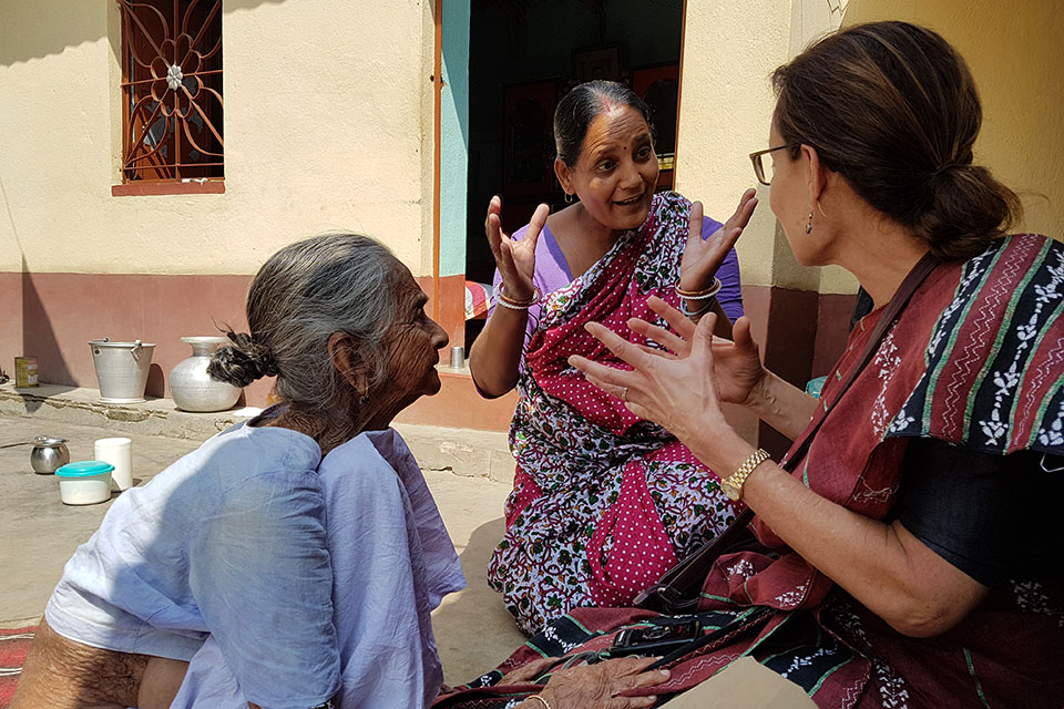 In an Indian village, a woman in a sari speaks with Professor Sarah Lamb while another older woman looks on.