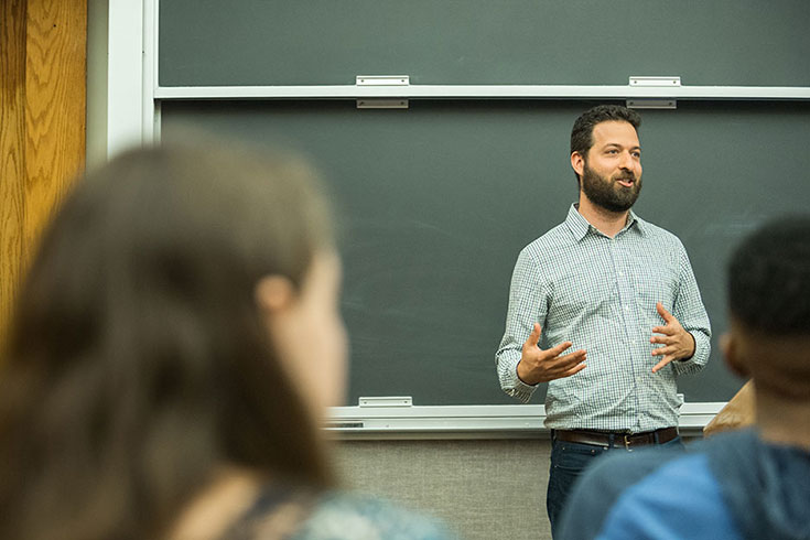 Jonathan Anjaria stands in front of a chalkboard, teaching