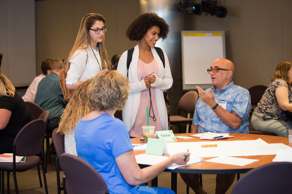 Teachers, some standing, some sitting, talking around a table