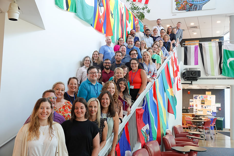 Photo of 2025 Summer Institute Cohort standing on long staircase surrounding by world flags