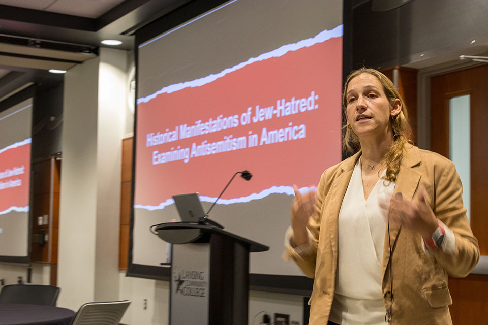 Photo of Rachel Fish teaching with slide in background titled "Historical Manifestation of Jew Hatred: Examining Antisemitism in America""