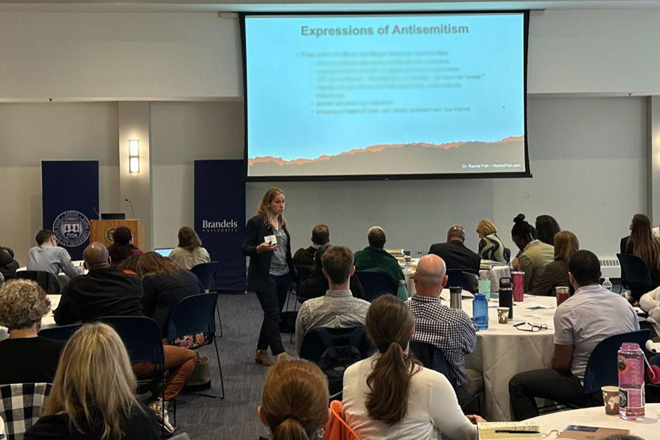 Rachel Fish, PhD, presenting in a room full of people with a slide on antisemitism in the background 