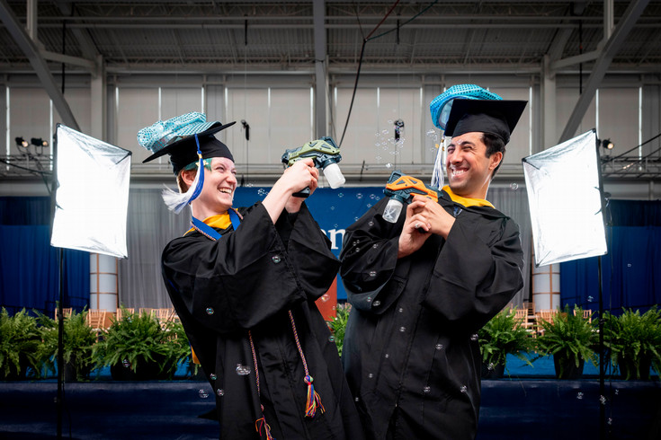 two students in graduation cap and gown celebrate at commencement