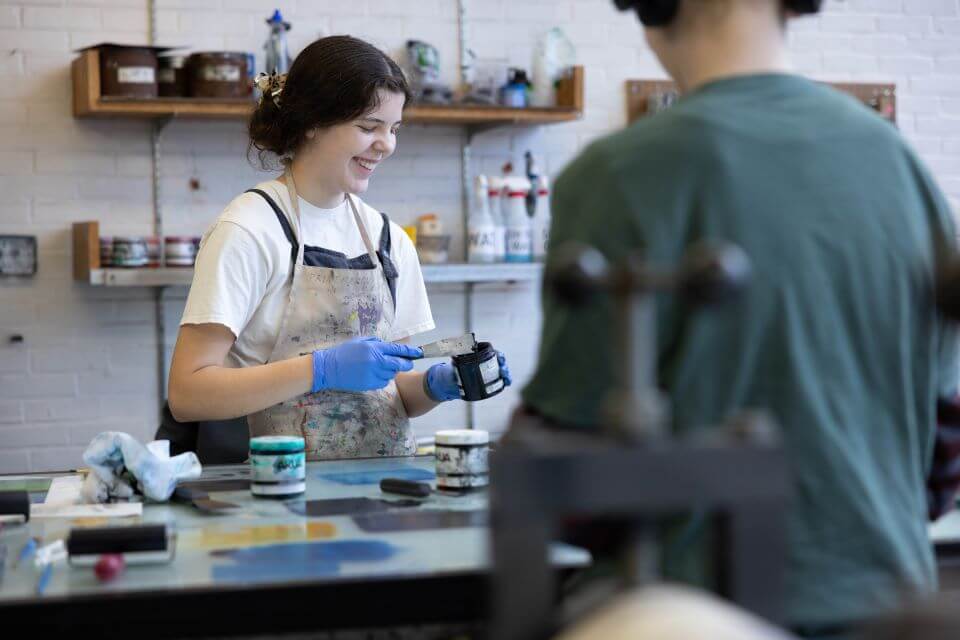 A person scoops paint from a jar while another person looks on