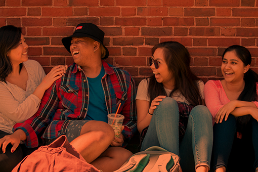 four students laughing together while seated on couch against brick wall