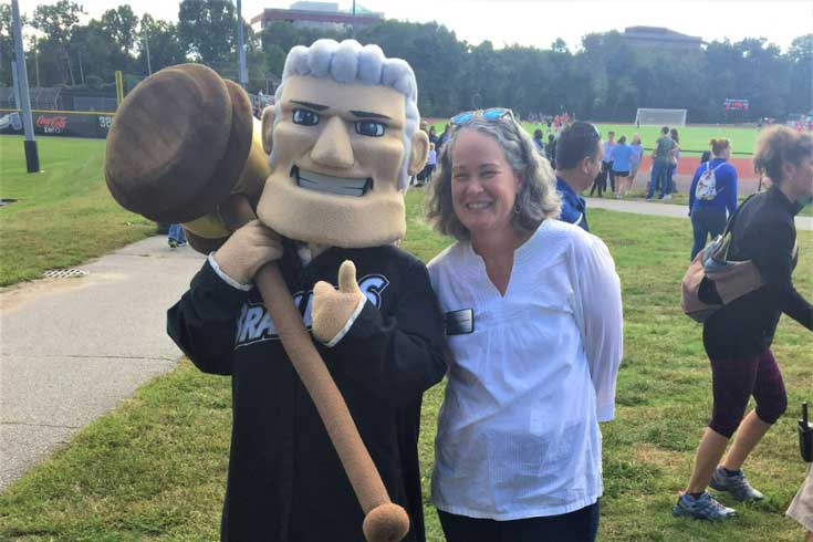 Dorothy, a white woman with curly grey hair, stands next to the Brandeis Judge mascot