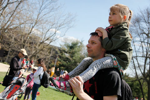 An adult with a child propped on his shoulders on the Great Lawn.
