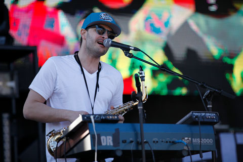 A member of Dale Earnhardt Jr. Jr. singing in front of a keyboard with a saxophone strung from his neck.
